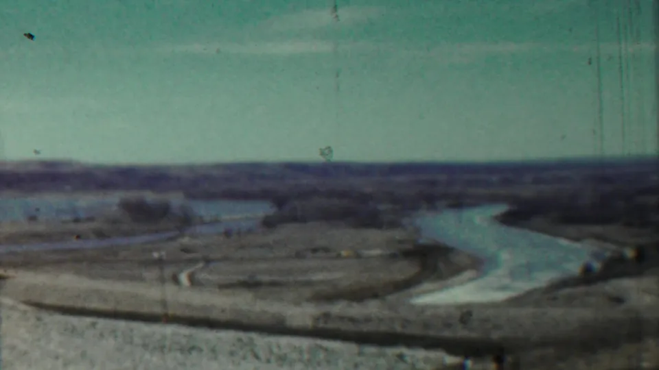 1959 8mm home-movie frame near Saint Francis, Kansas, showing a winding river through open countryside beneath a pale sky.