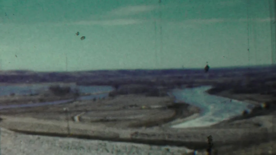 Wide 1959 Kansas countryside view with a river bend, low banks, sparse trees, and visible vertical wear in the 8mm frame.