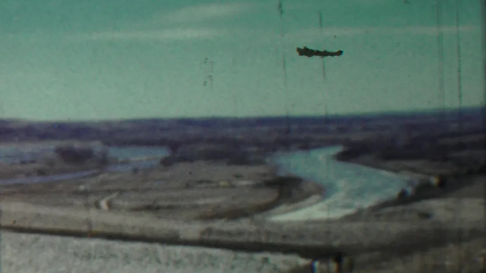 Final 1959 8mm frame of the Saint Francis countryside, with the winding river visible below a pale sky and a dark film artifact overhead.