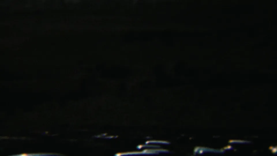 Dark 8mm frame with an indistinct landscape or parking-area edge and a few small bright shapes near the bottom.