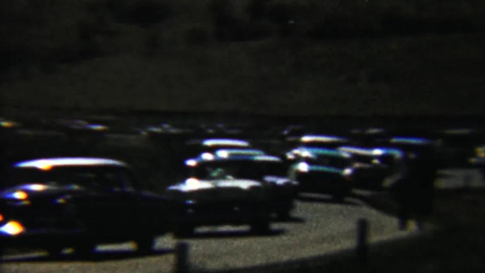 1959 Saint Francis, Kansas home-movie frame showing dark late-1950s cars clustered on a winding road at night.