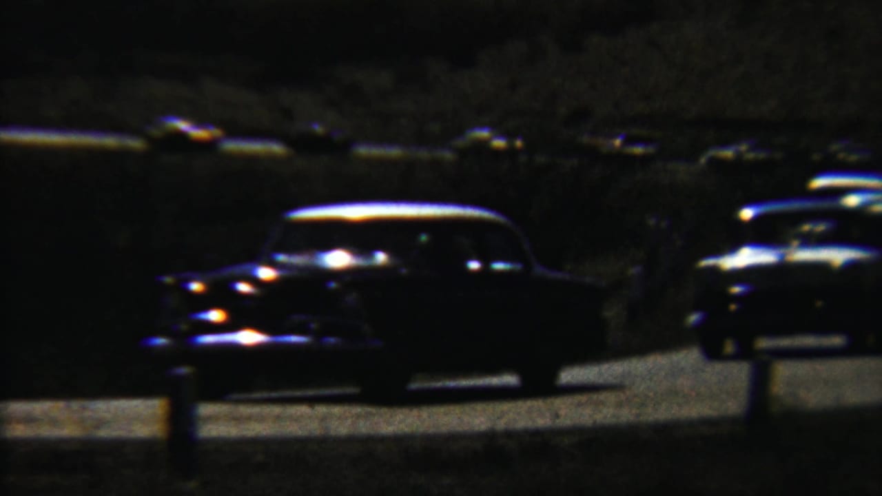 Cars sit along a dark road while a small figure stands near the traffic.