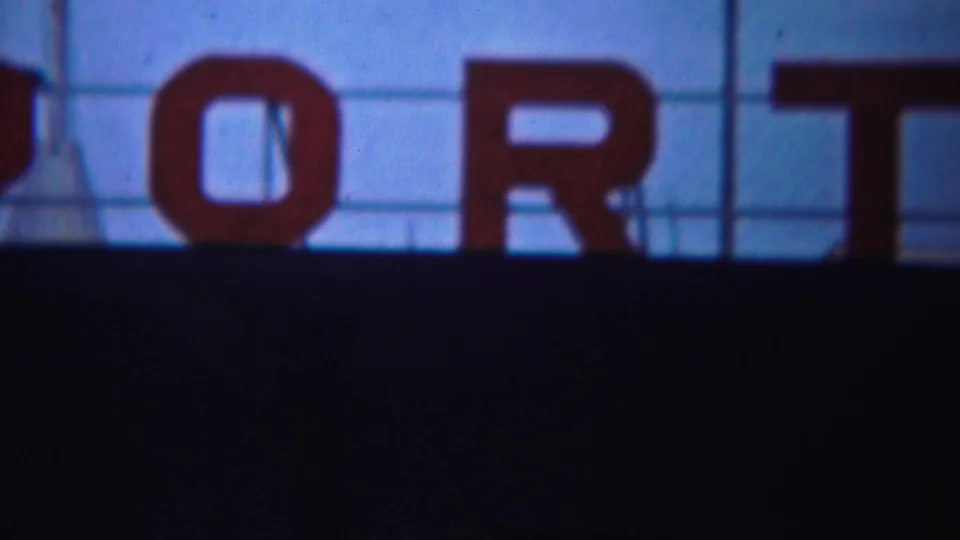 1954 Yokohama home-movie frame showing partial red PORT lettering above a dark foreground and blue sky.