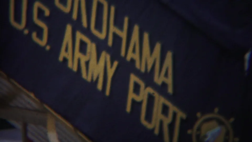 Close 8mm frame of Yokohama U.S. Army Port lettering on a dark blue sign, with soft focus and grain.