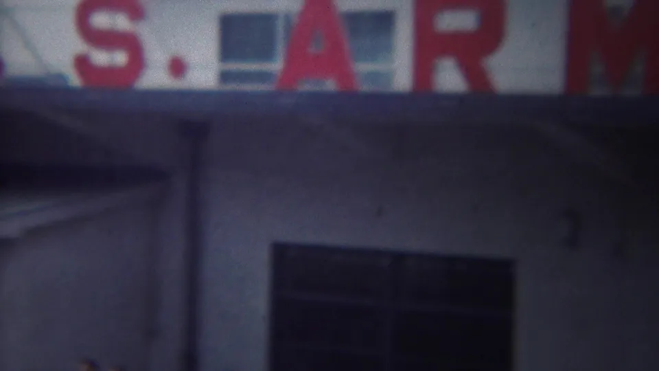 Final 1954 frame holds on the Yokohama U.S. Army port facade, showing red sign letters, white wall, and dark windows.