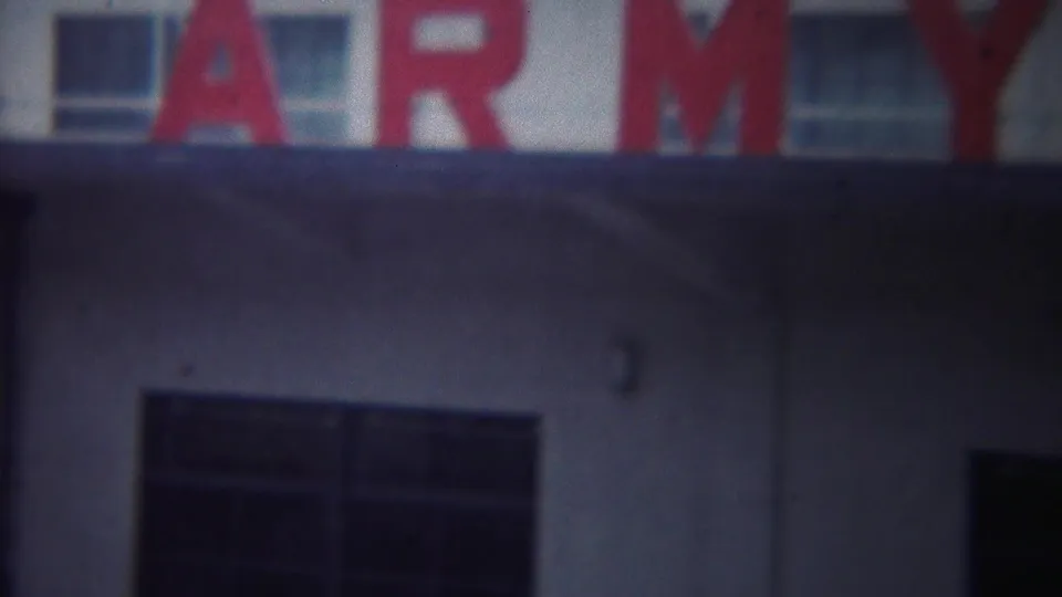 1954 Yokohama home-movie frame showing part of a red Army Port sign across a pale building facade.
