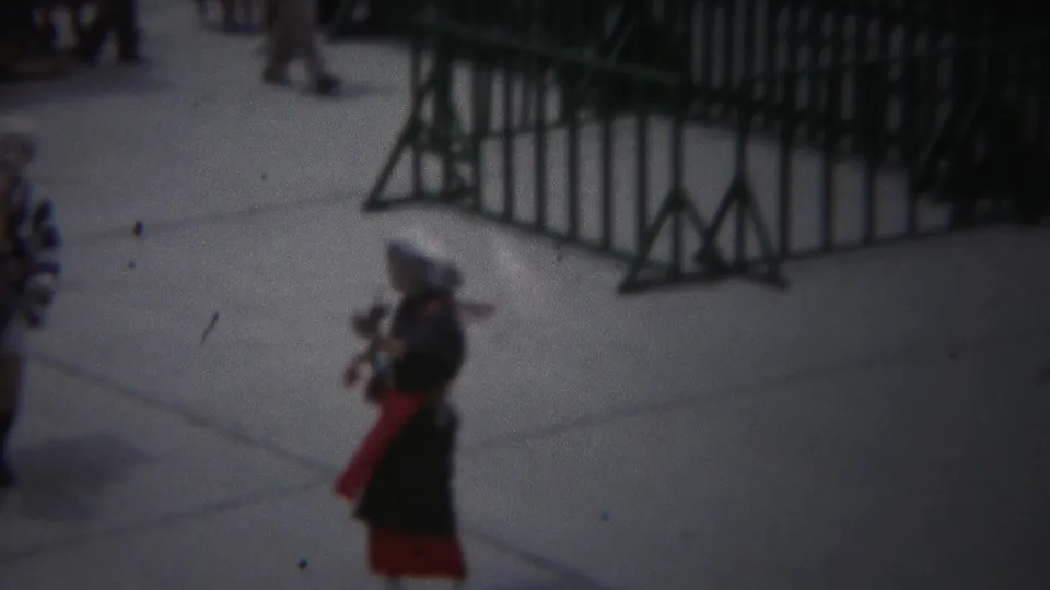 1954 Yokohama frame of a robed performer holding an instrument beside metal street barriers.