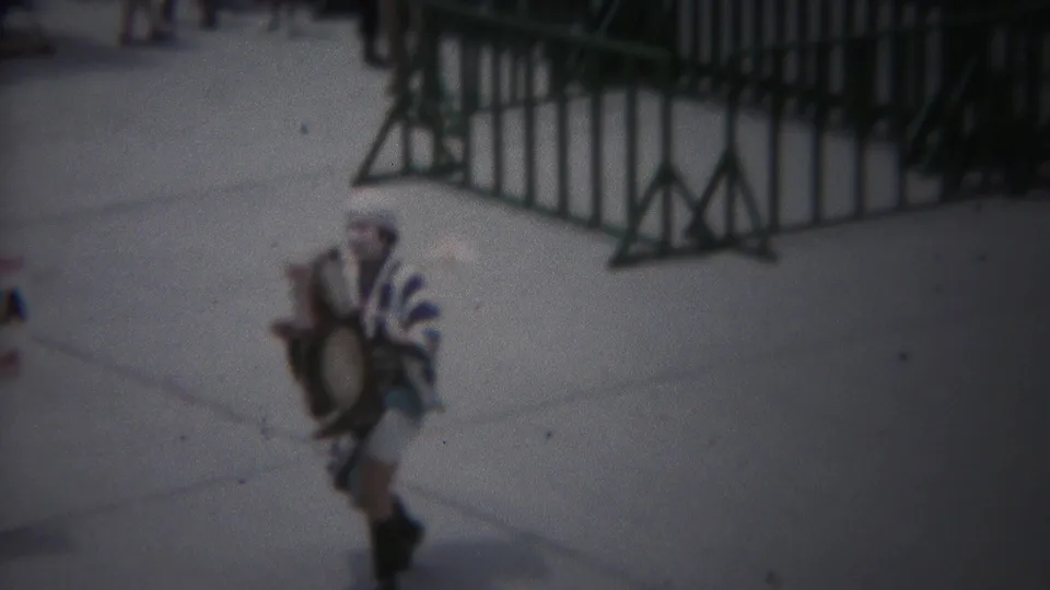 1954 Yokohama frame showing a striped-costume performer with a drum-like instrument on a barricaded walkway.