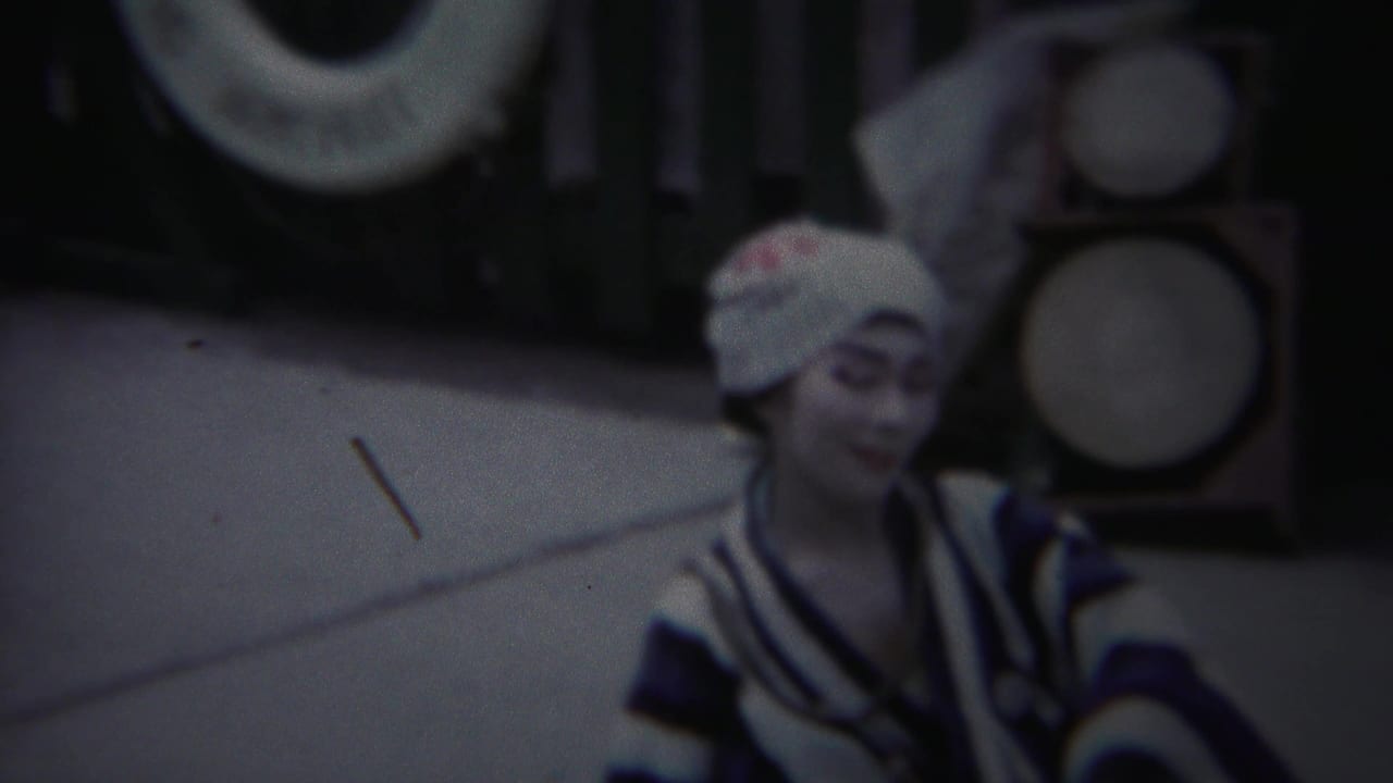 The Yokohama performer appears in closer view, her painted face and striped kimono visible against drums or circular props.