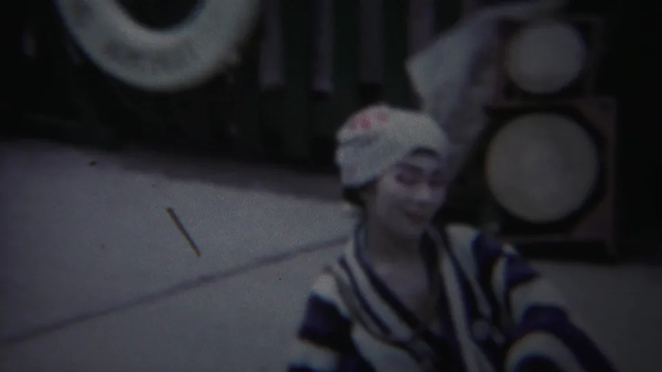 The Yokohama performer appears in closer view, her painted face and striped kimono visible against drums or circular props.