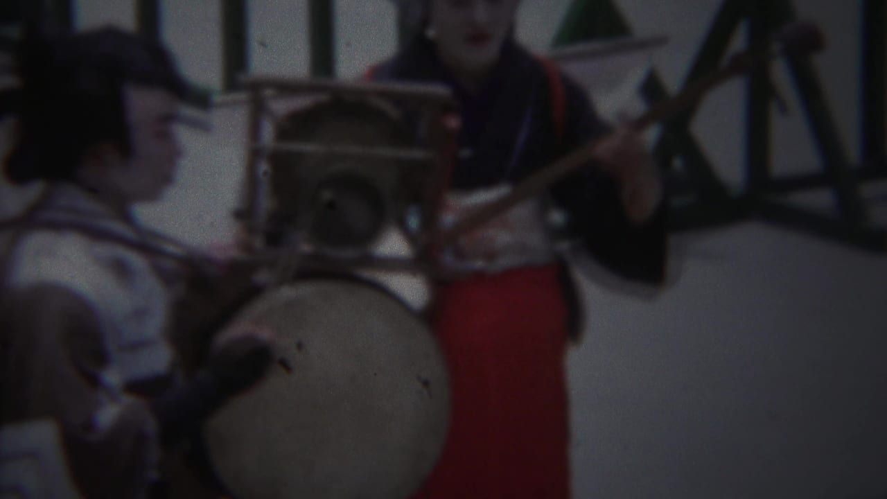 1954 Yokohama home-movie frame showing performers in traditional-style costume with a large drum and shamisen-like instrument.