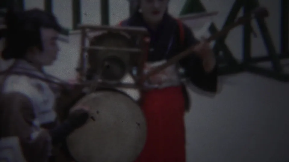 1954 Yokohama home-movie frame showing performers in traditional-style costume with a large drum and shamisen-like instrument.