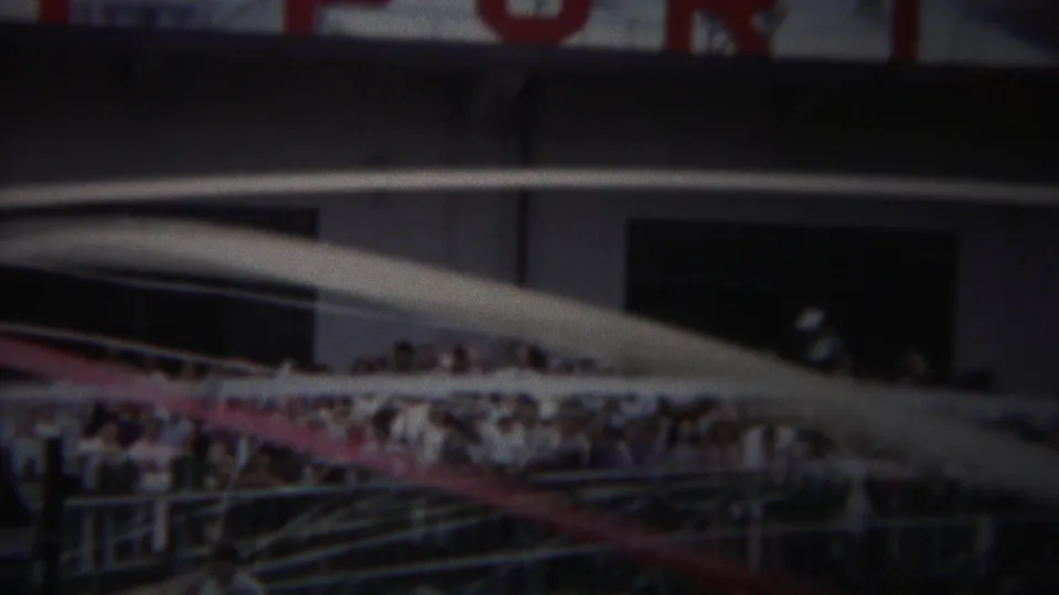 Yokohama 1954 home-movie frame showing spectators behind railings near classic cars and a large venue or industrial building.