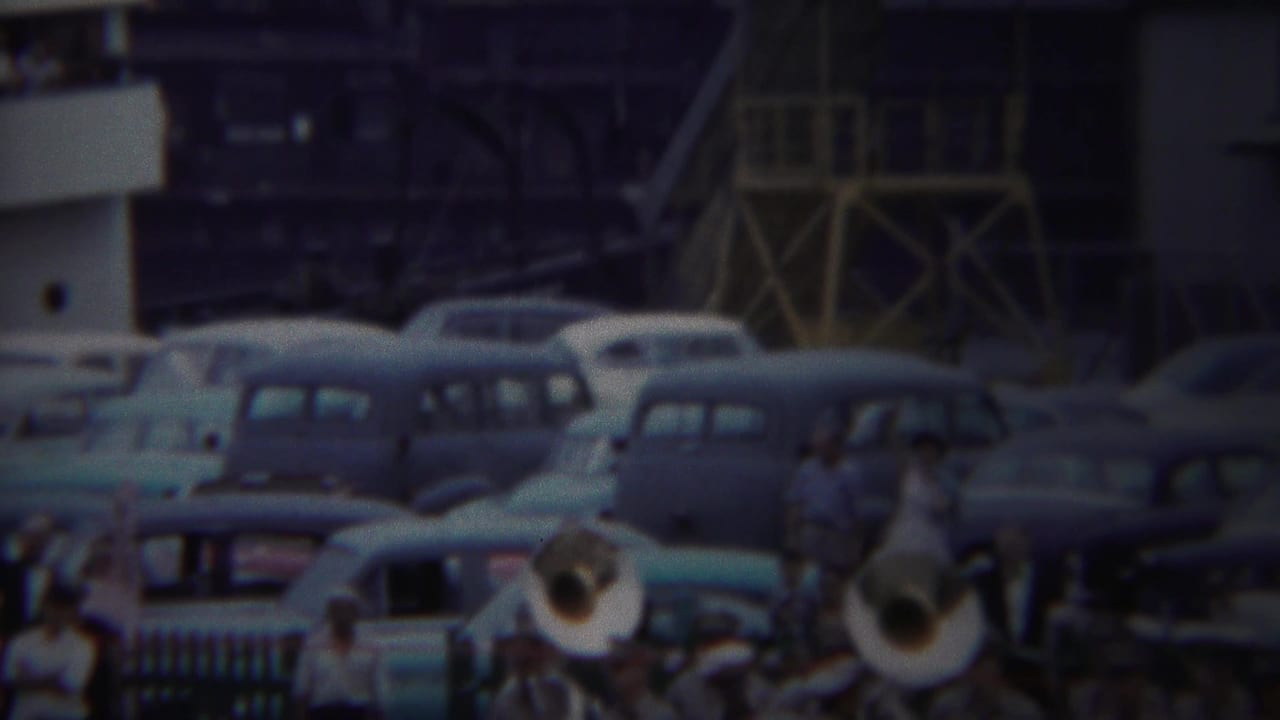 Yokohama 1954 home-movie frame with brass players in the foreground, rows of classic cars, and spectators above or behind railings.
