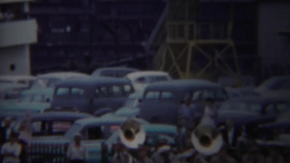 Yokohama 1954 home-movie frame with brass players in the foreground, rows of classic cars, and spectators above or behind railings.