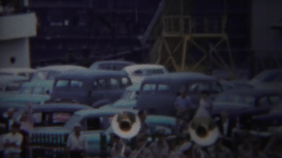 Yokohama, Japan, 1954 home-movie frame of a brass band performing beside parked cars and onlookers at an army port.
