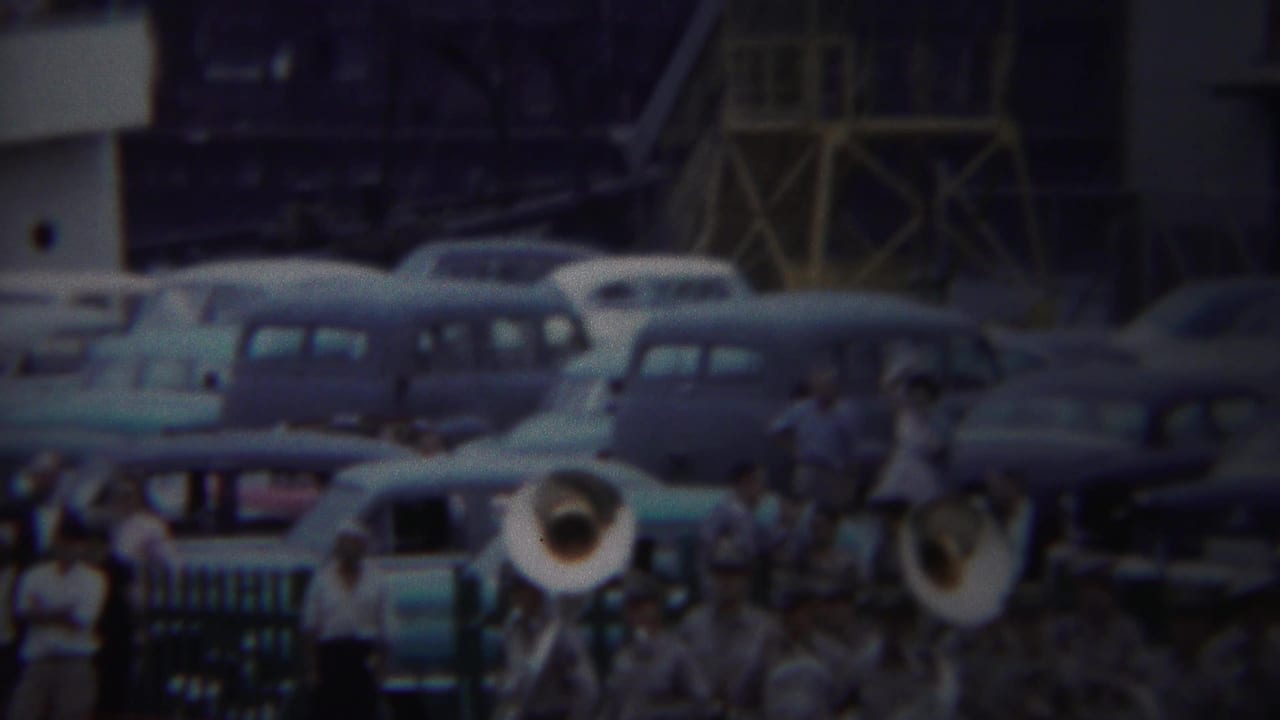 1954 Yokohama army port frame with uniformed musicians, brass instruments, spectators, and parked cars in soft 8mm color.