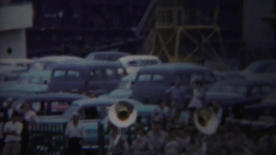 1954 Yokohama army port frame with uniformed musicians, brass instruments, spectators, and parked cars in soft 8mm color.