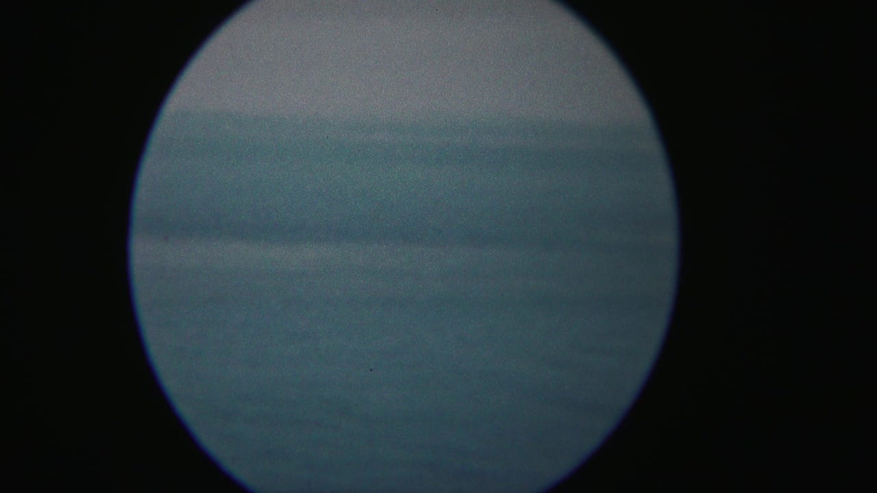 1954 Yokohama home-movie frame with a circular lens view over blue-gray water, haze, and a faint distant shoreline.