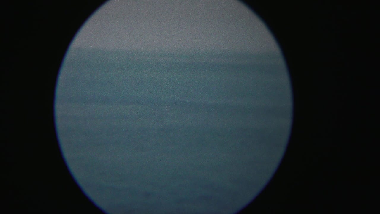 A blue-toned 1954 Yokohama waterfront view appears through circular vignetting, with soft haze and indistinct distance.