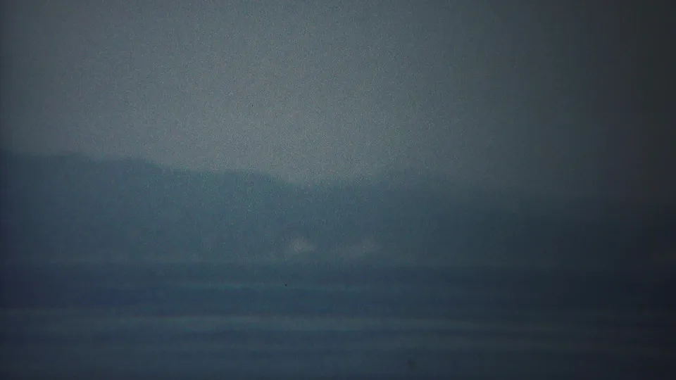 1954 Yokohama-area home-movie frame showing calm blue water, a fog-softened horizon, and faint distant shore.