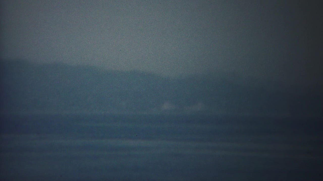 Soft, darkened horizon over calm blue water in haze.