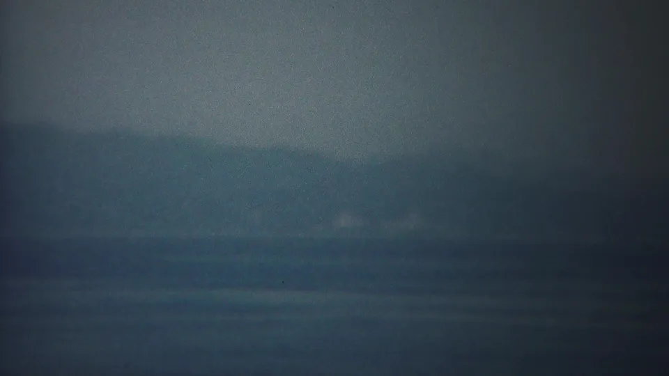 Hazy 1954 Yokohama sea view with indistinct landforms and calm water beneath a dim sky.