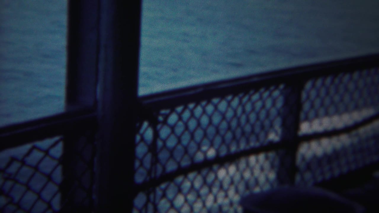 Shipboard or pier-side chain-link railing frames calm water in this hazy 1954 Yokohama travel shot.