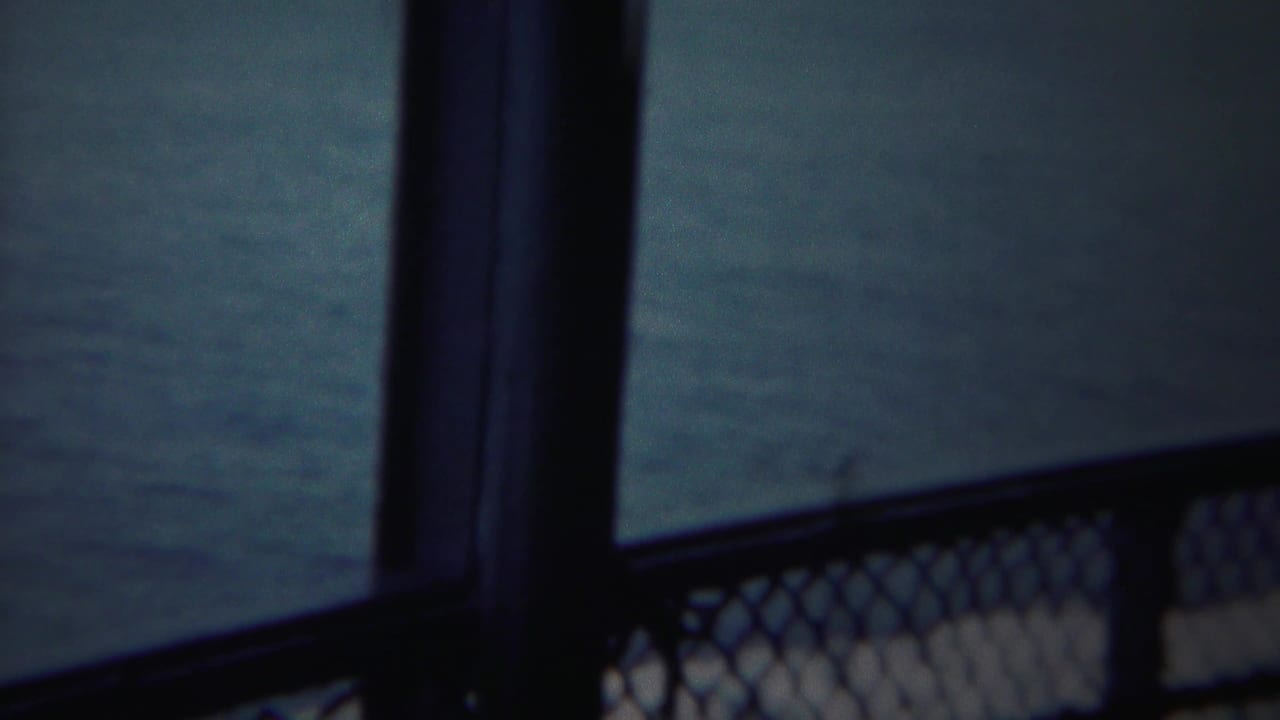 Blue-tinted 8mm frame showing chain-link railing and dark ship structure over open water near Yokohama.