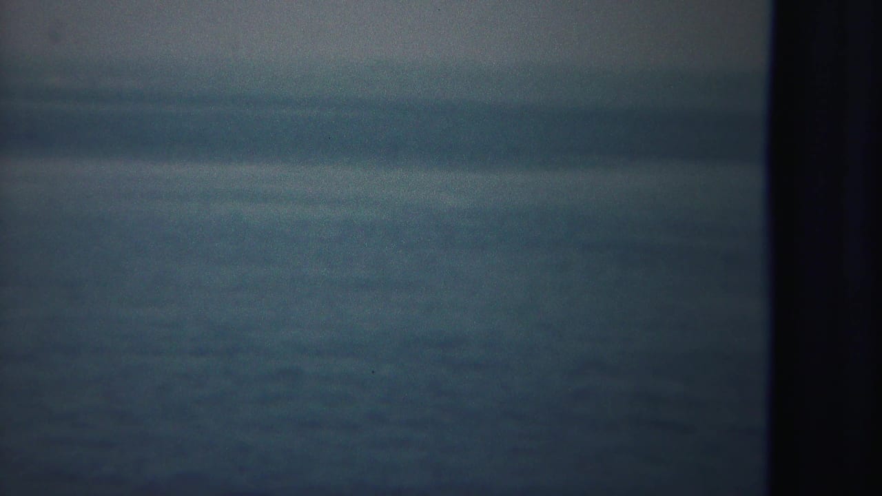 Soft-focused 8mm view of open water from a moving vessel, with a dark ship post along the right side.
