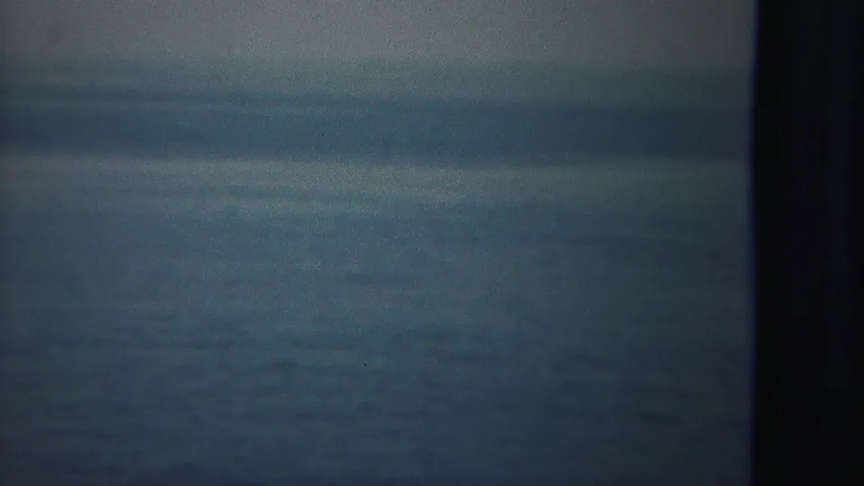 Soft-focused 8mm view of open water from a moving vessel, with a dark ship post along the right side.