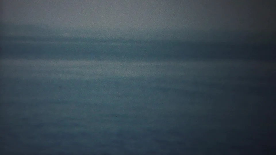 A subdued 8mm coastal view near Yokohama, with calm water, haze, and a vertical scan or frame join through the center.