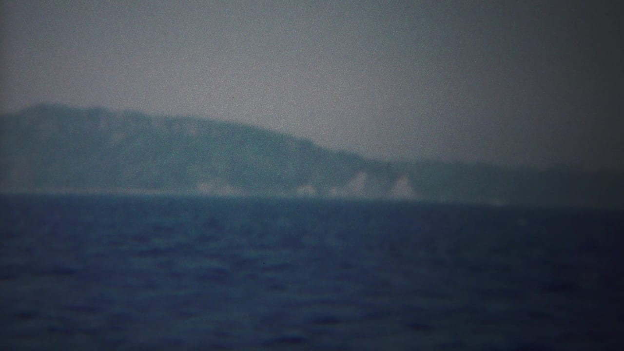 1954 Yokohama coastal frame showing open water in the foreground and hazy hills or mountains along the distant shoreline.