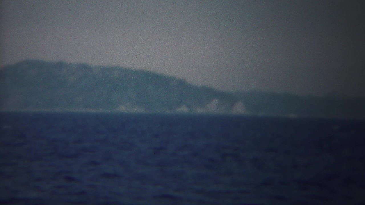 A blue-gray 8mm view of Yokohama waters with distant hills, faint shoreline detail, and soft atmospheric haze.