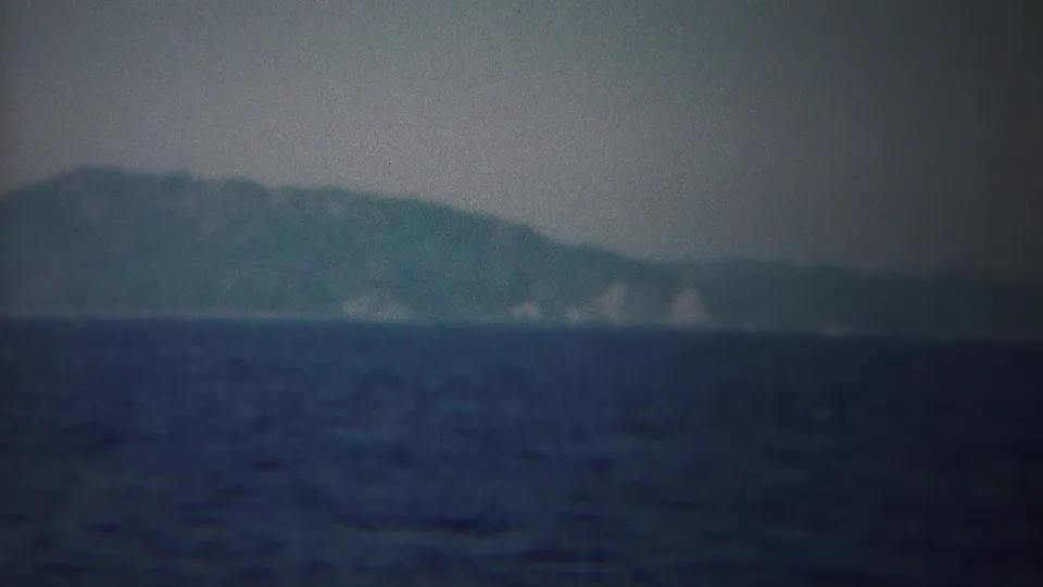 1954 8mm view near Yokohama, Japan, showing dark open water and a soft, hazy shoreline on the horizon.