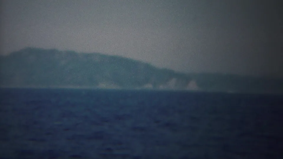 Soft 8mm frame of a distant landmass near Yokohama, with pale shoreline areas visible beyond the open sea.
