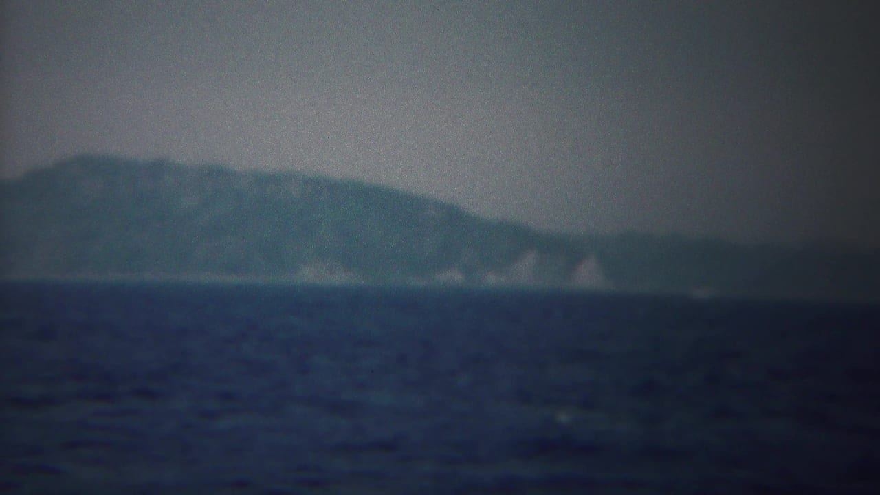 Vintage 8mm boat-view frame showing open water and a low, blurred shoreline near Yokohama, Japan.