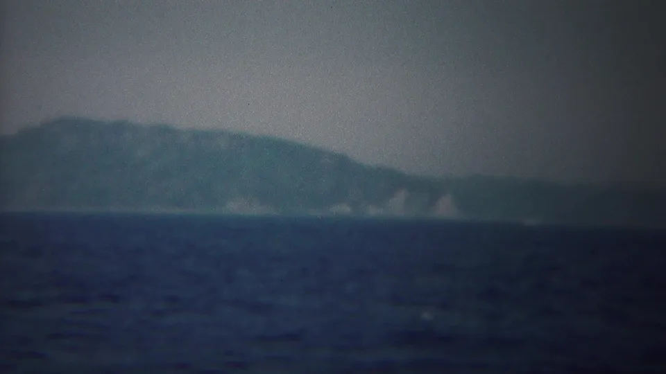 Vintage 8mm boat-view frame showing open water and a low, blurred shoreline near Yokohama, Japan.