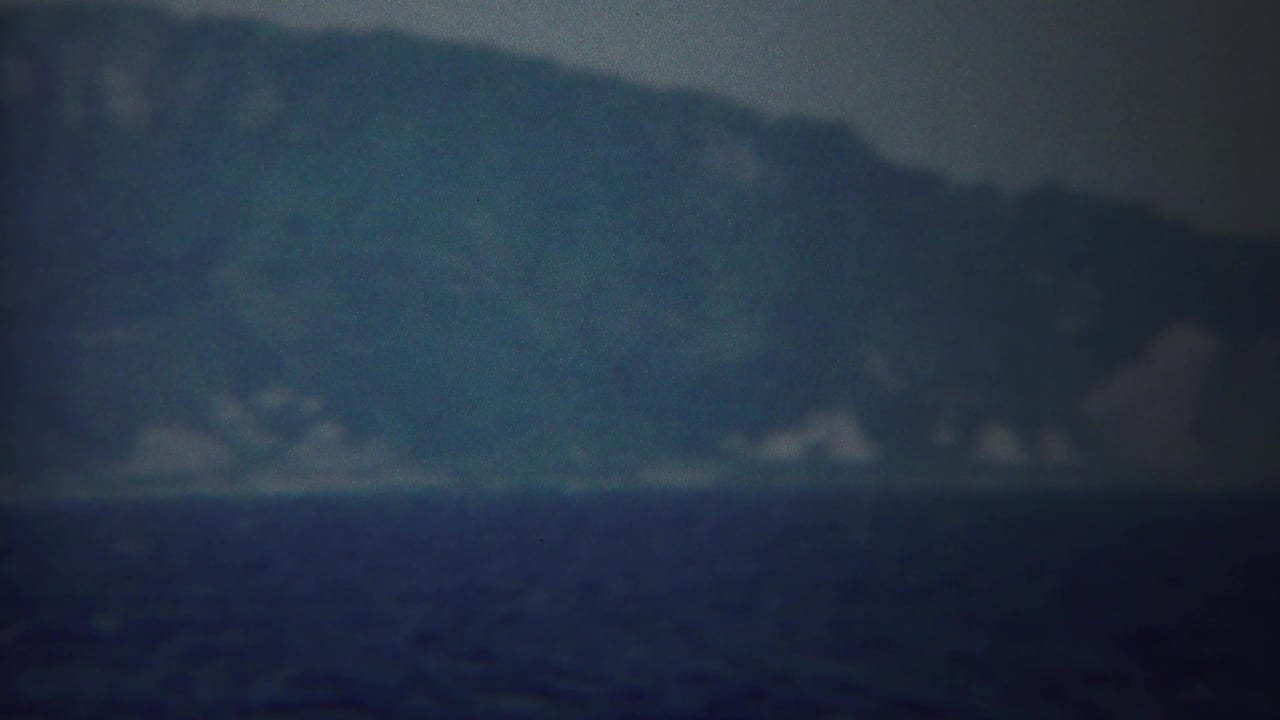 Hazy mountains across dark water with a soft blue-green 8mm film look.