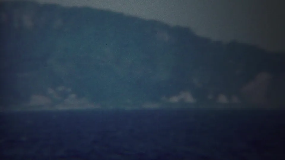 Distant mountains and shoreline across the water in 1954 Yokohama home-movie footage, softened by haze and grain.