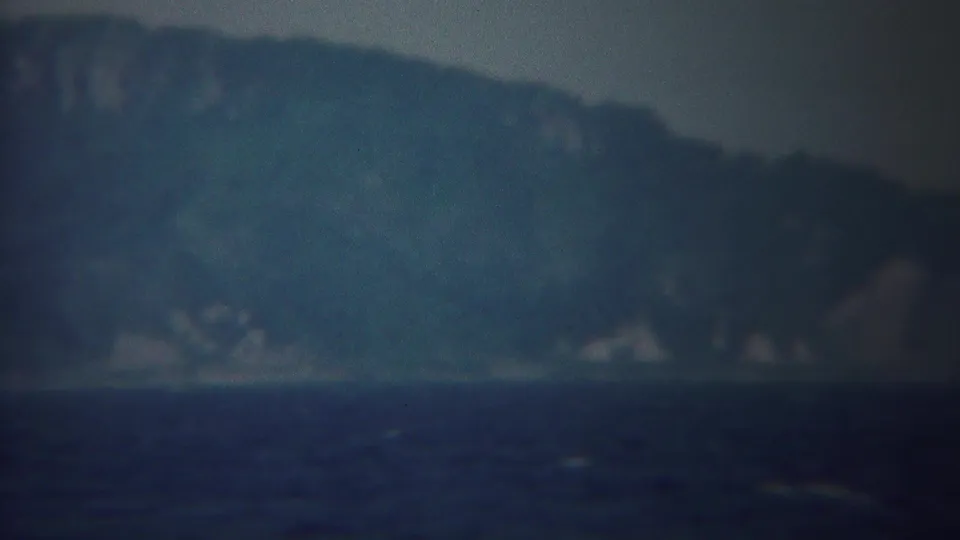 A hazy Yokohama coastal view shows dark water, distant mountains, and a small bird-like speck in soft 8mm footage.