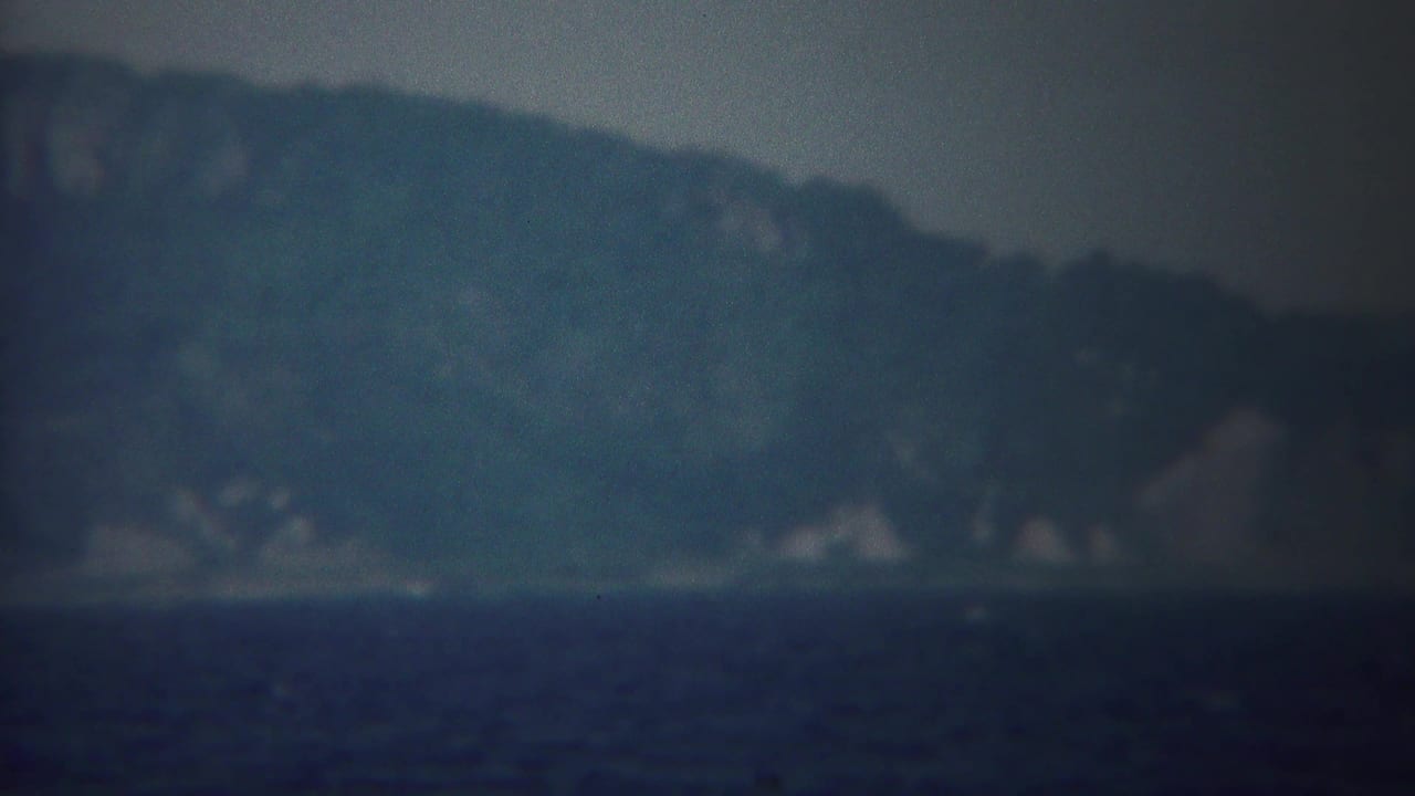 The 1954 Yokohama seascape continues with misty mountains, a low shoreline, and dark water in muted 8mm color.