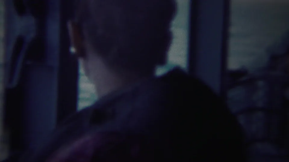A person viewed from behind looks out toward the Yokohama water and distant coast, partially framed by a window or boat structure.