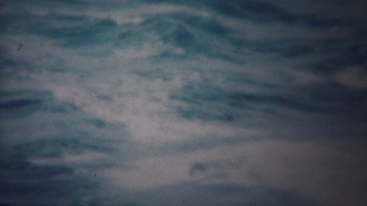 Grainy 1954 Yokohama 8mm frame showing dark blue-gray sea water and white foam moving across the surface.