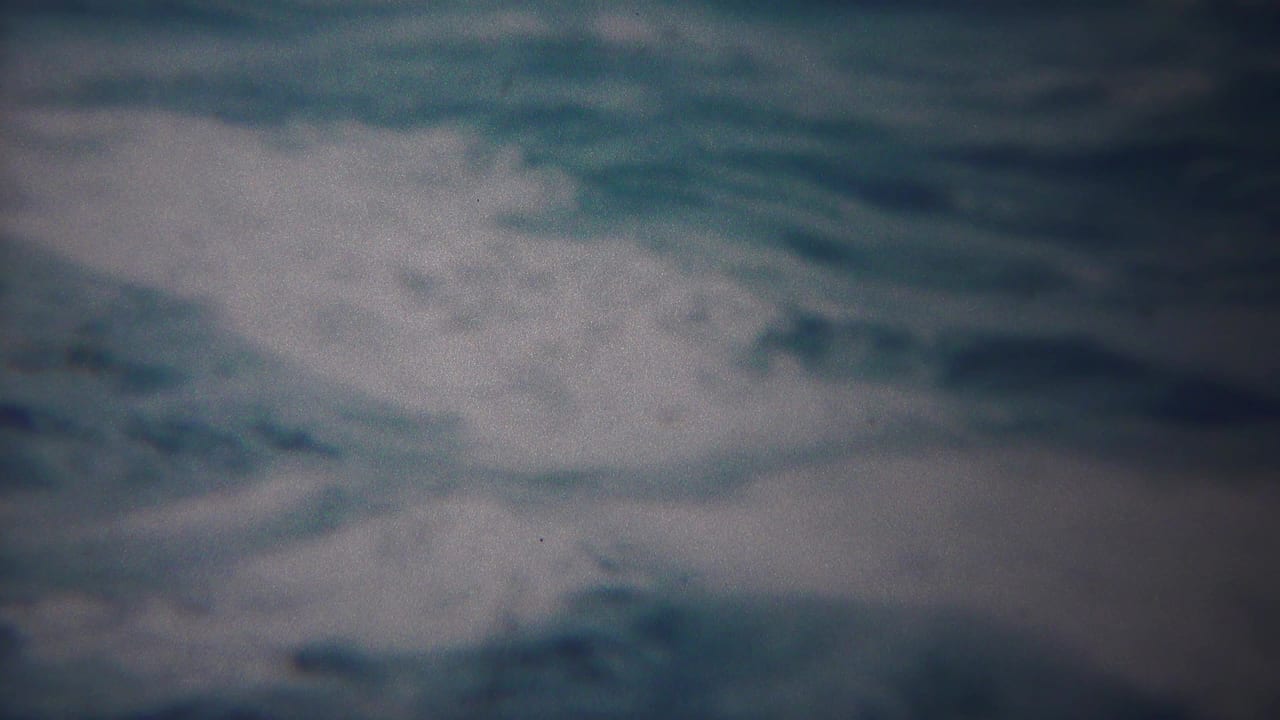 1954 Yokohama home-movie frame with turbulent blue-gray water and a wide white foam break near the upper right.