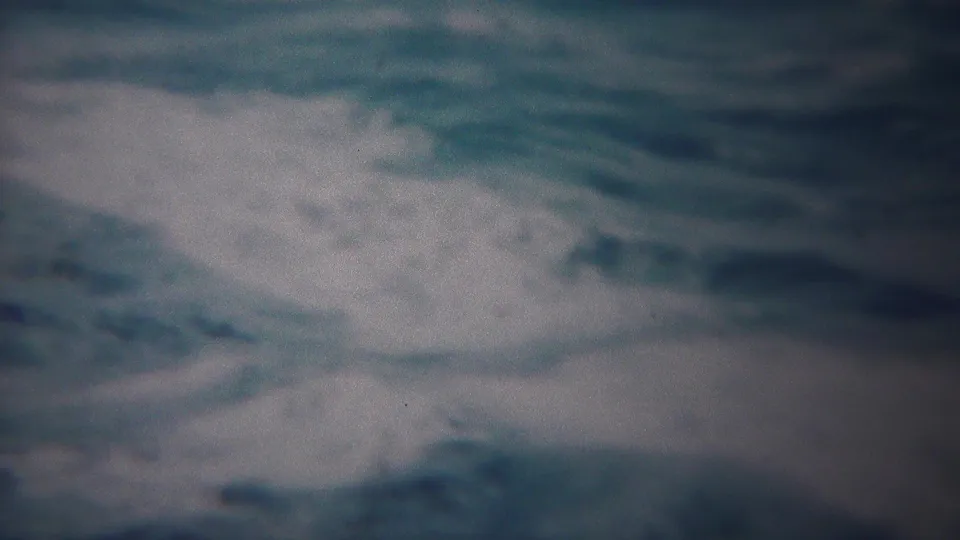 1954 Yokohama home-movie frame with turbulent blue-gray water and a wide white foam break near the upper right.