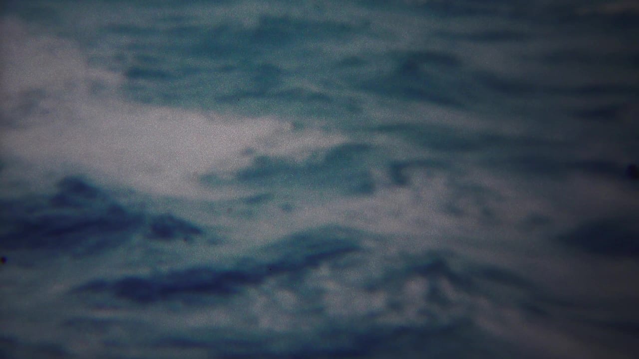 Grainy 8mm frame from Yokohama showing rough ocean texture, white foam streaks, and soft blue-gray color.