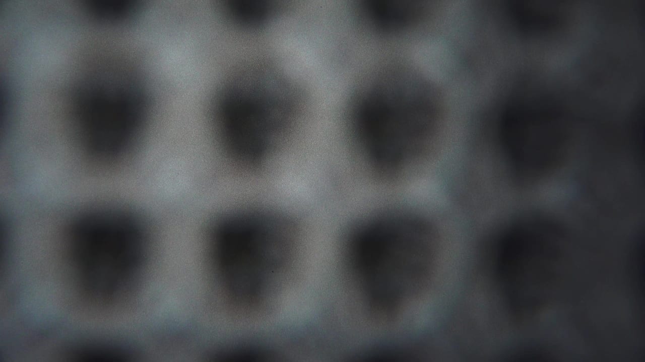 1954 Yokohama 8mm frame with rows of dark rounded holes or pits on a grey patterned field, seen in shallow focus.