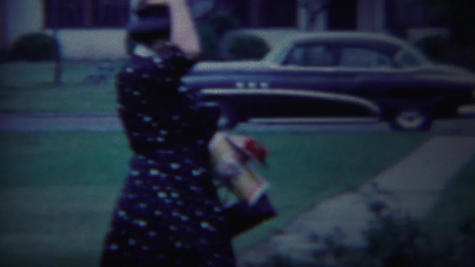 Side view of the woman walking along a South Bend sidewalk, carrying an item as a mid-century car remains parked nearby.