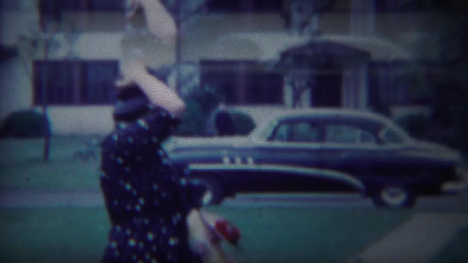 The woman continues down the South Bend sidewalk, framed by a residential house, lawn, small trees, and a parked 1950s sedan.